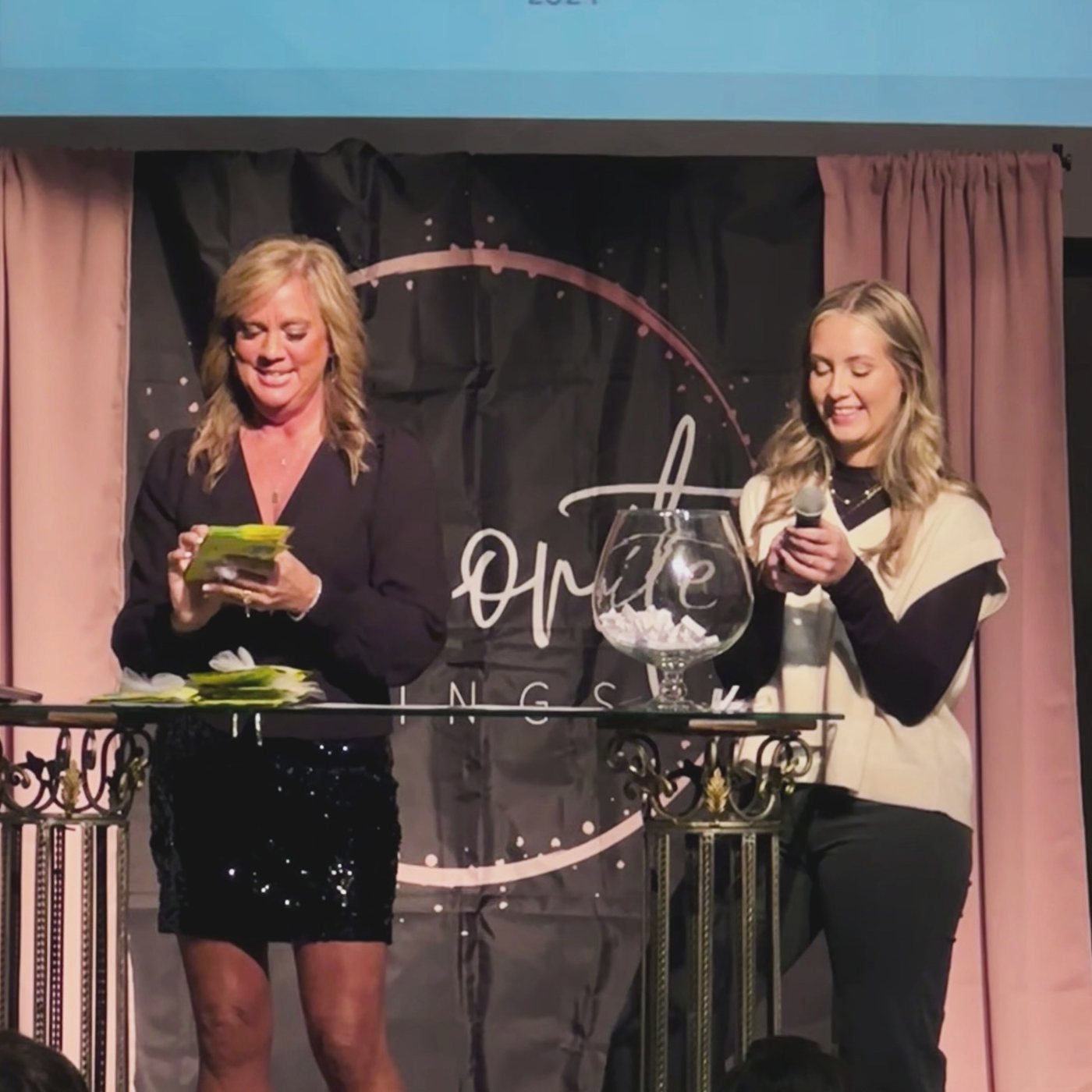 Danielle and Sadie drawing door prizes on stage