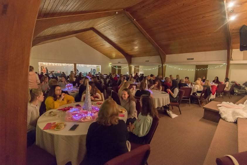 A full room of women at round tables during the evening